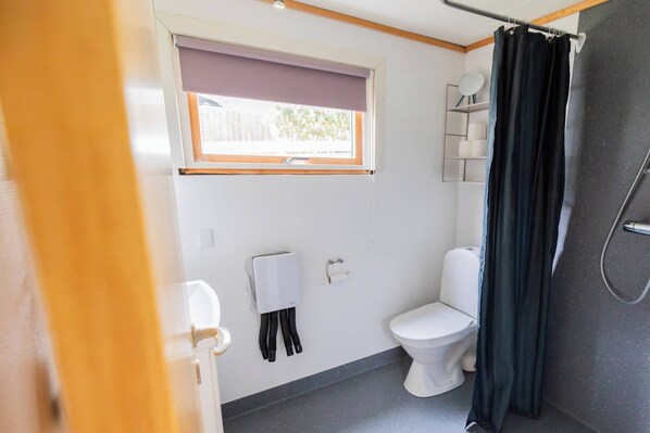 Un baño pequeño con inodoro, cortina de ducha y ventana con persiana.