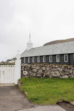 A church with a stone wall and a white fence in front. - Traditional Faroese House Near Airport (Sørvágur)