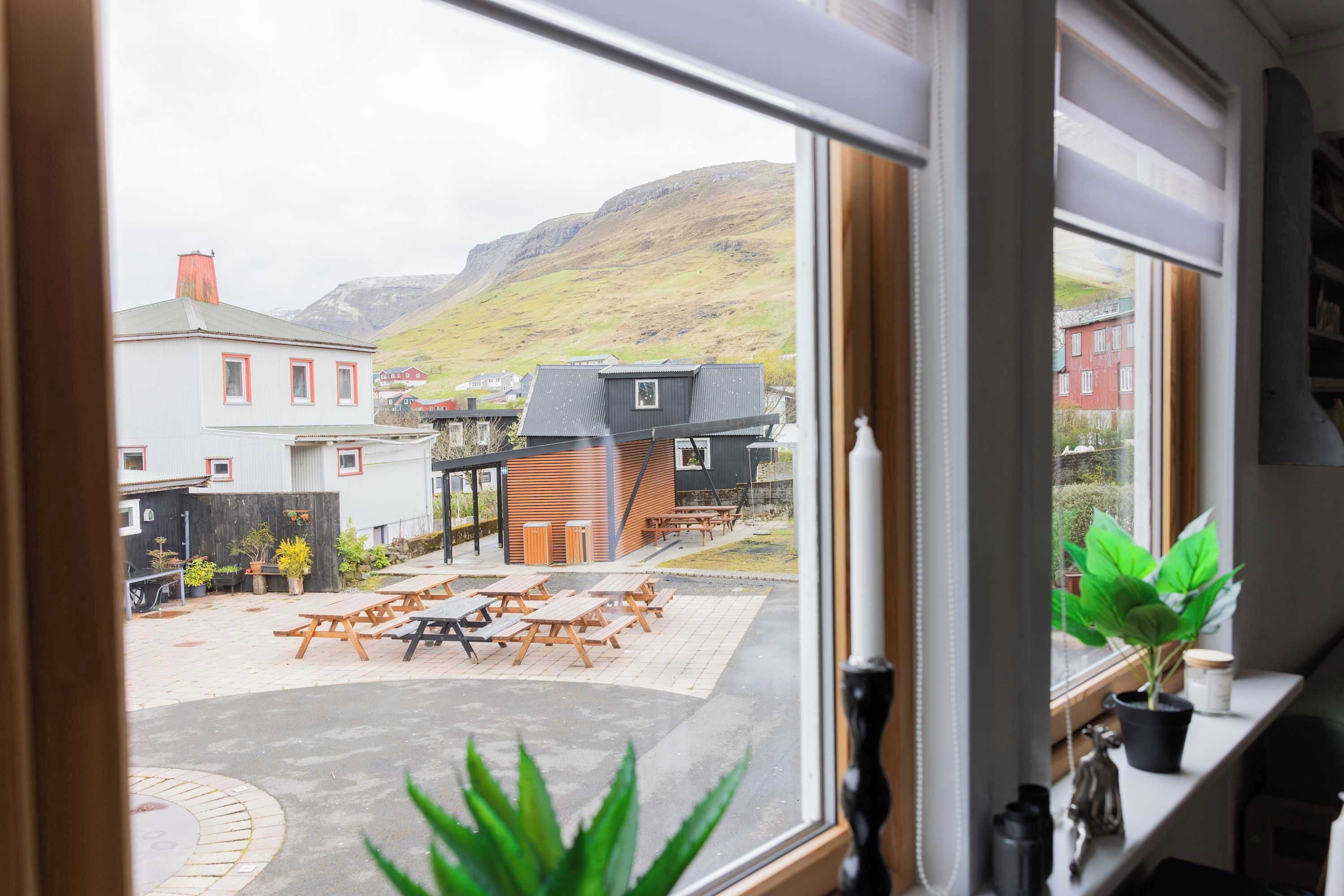 A view from a window of a building with a patio area, outdoor seating, and a mountain in the background.