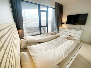 A hotel room with two beds, a TV, and a window with a view of the city. - Modern 4BR Luxury Home with Ocean View & Jacuzzi (Sandavágur)