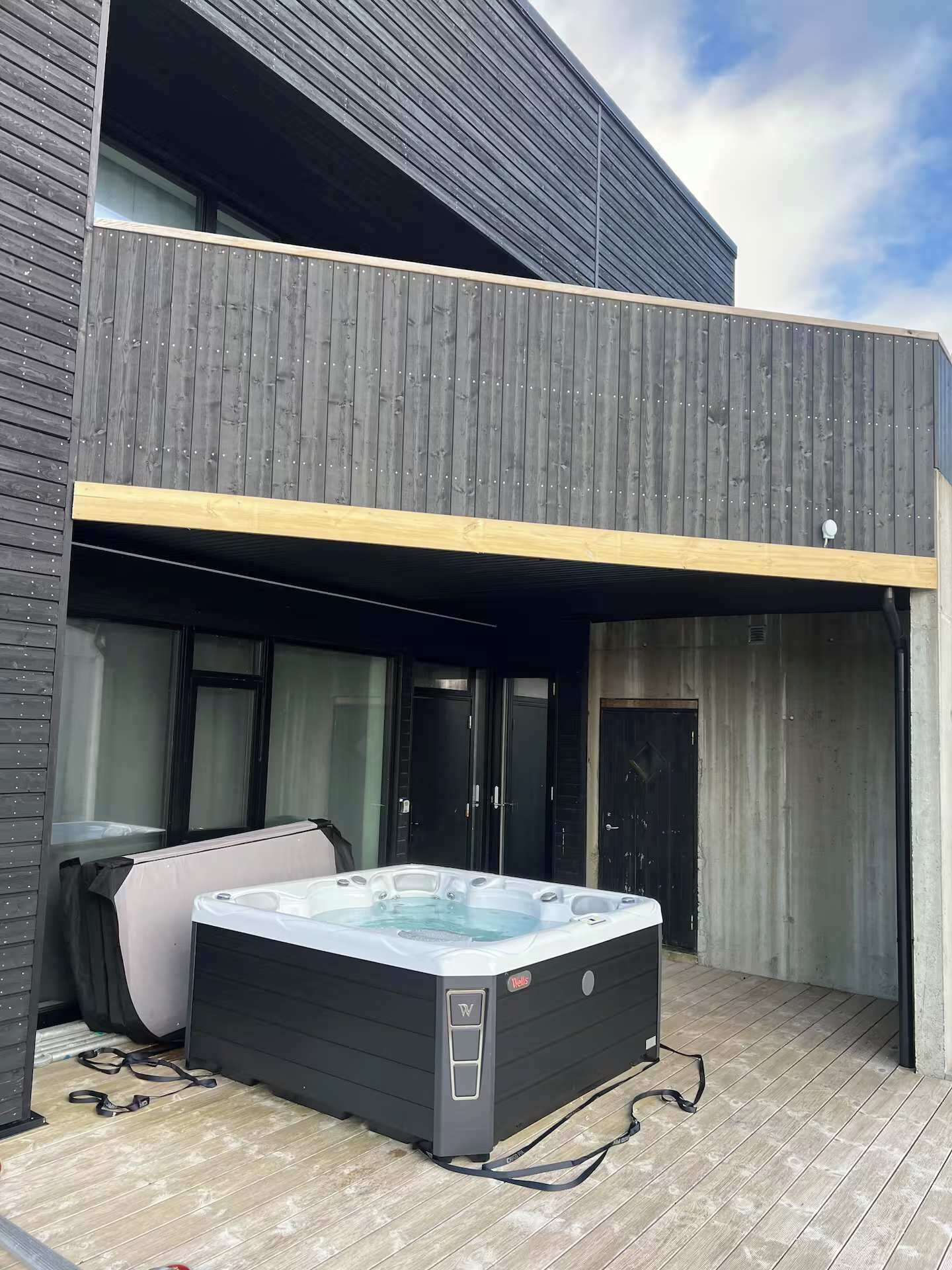 A modern building with a wooden exterior, a covered patio area, and a hot tub.