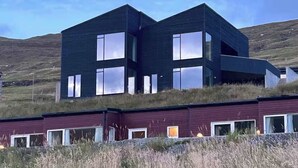 Un bâtiment moderne à deux étages, doté de grandes fenêtres et d’un toit plat, situé sur une colline verdoyante.
