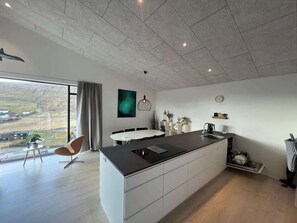 A modern kitchen with a large island, a dining area, and a view of the countryside. - Modern 4BR Luxury Home with Ocean View & Jacuzzi (Sandavágur)