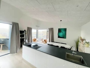 A modern kitchen with a central island, dining area, and large windows offering a view.