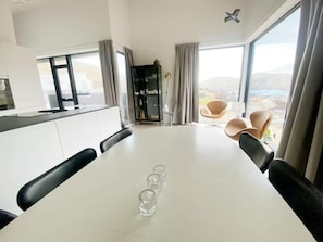 A modern dining area with a white table, black chairs, and a view of the outdoors through large windows.