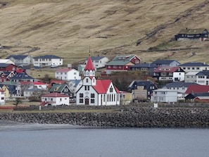 A coastal town with a prominent church featuring a red roof and white walls, surrounded by residential buildings with varied roof colors.