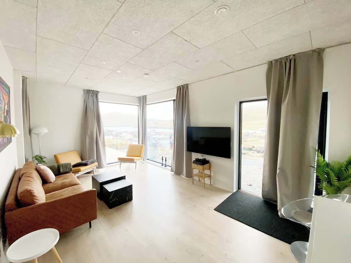 En moderne stue med sofa, sofabord, fjernsyn og udsigt til det fri.