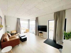 Una sala de estar moderna con un sofá, una mesa de centro, un televisor y vistas al exterior.