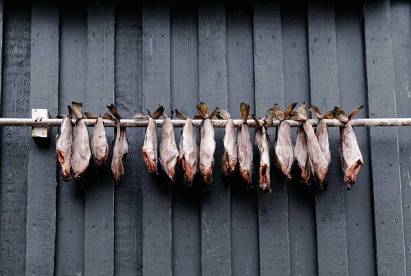 Filetta di pesce essiccato appese a una mensola di legno su uno sfondo di parete in legno scuro.