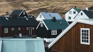 A mountain with a snow-capped peak in the background, surrounded by houses with green roofs. - Relaxed Stay with Fjord Views in Hvalvik (Hvalvík)