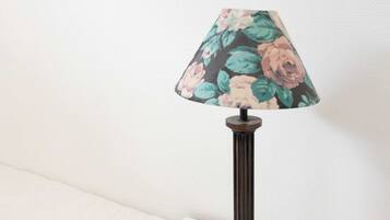 Une lampe de table avec un abat-jour à motifs floraux, posée sur une table blanche devant un mur uni.