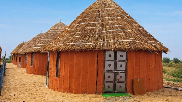 Een rij rieten hutten met een centrale deur, gelegen in een zandrijk gebied.