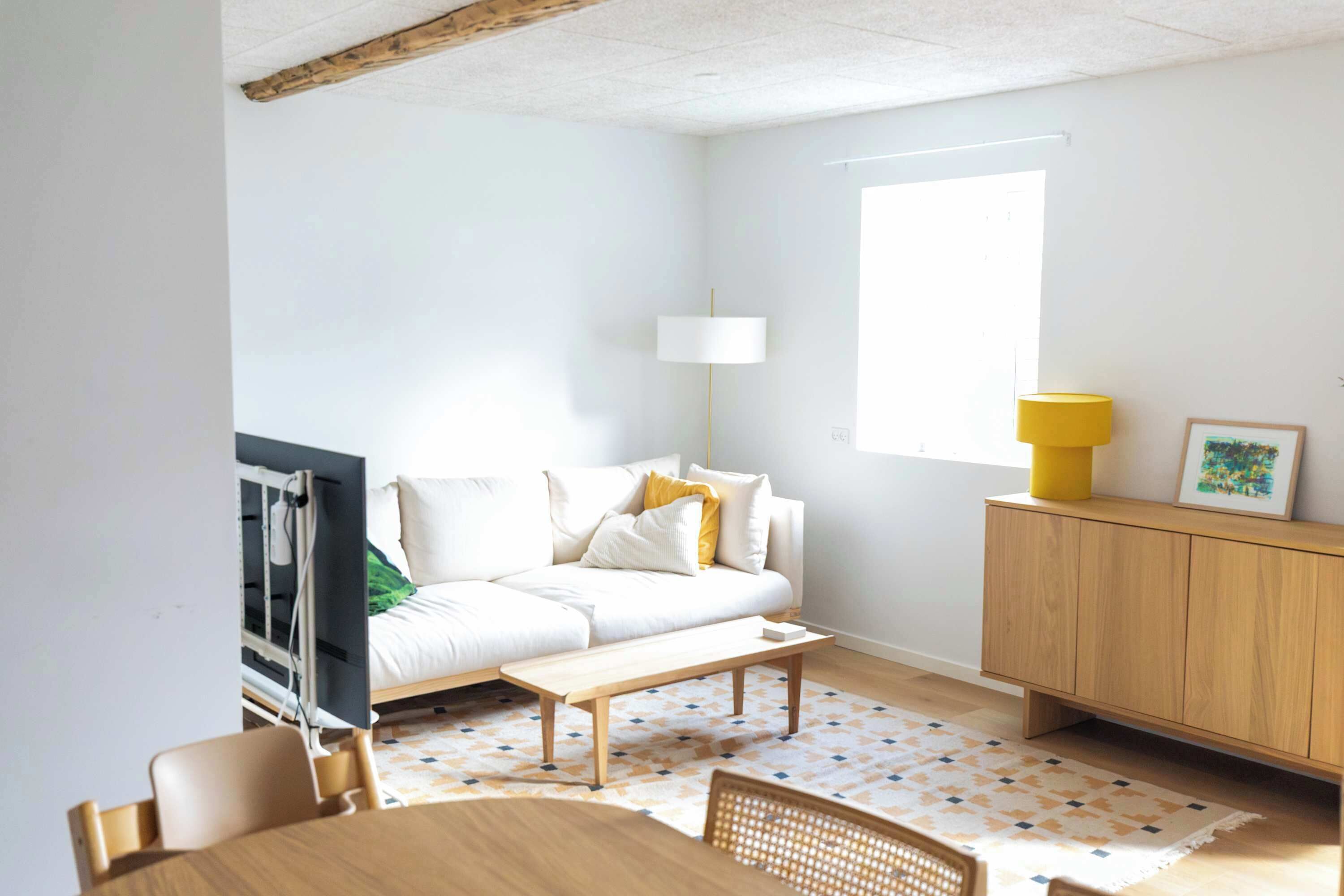 Uma sala de estar moderna com sofá, mesa de centro de madeira, mesa de jantar com cadeiras, armário e janela que oferece iluminação natural.
