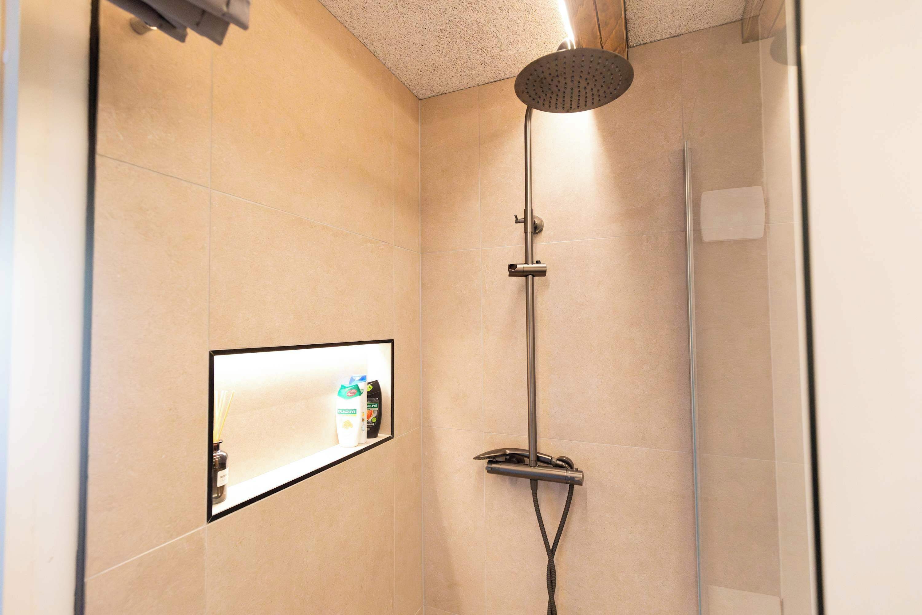 Eine moderne Dusche mit Handbrause, Bedienfeld an der Wand und Glastür.