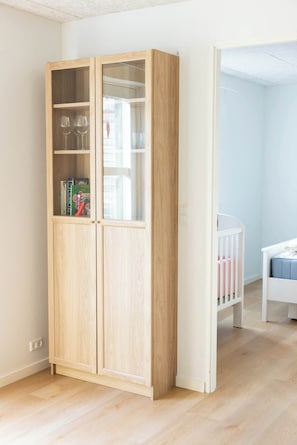 Una habitación con un armario de madera, una cuna y una cama blanca.