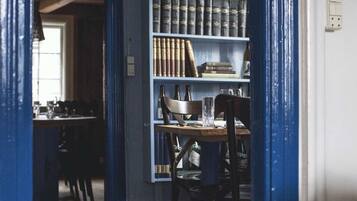 Una habitación con piso de madera, una mesa de comedor con sillas, una estantería llena de libros y una pared pintada de azul.