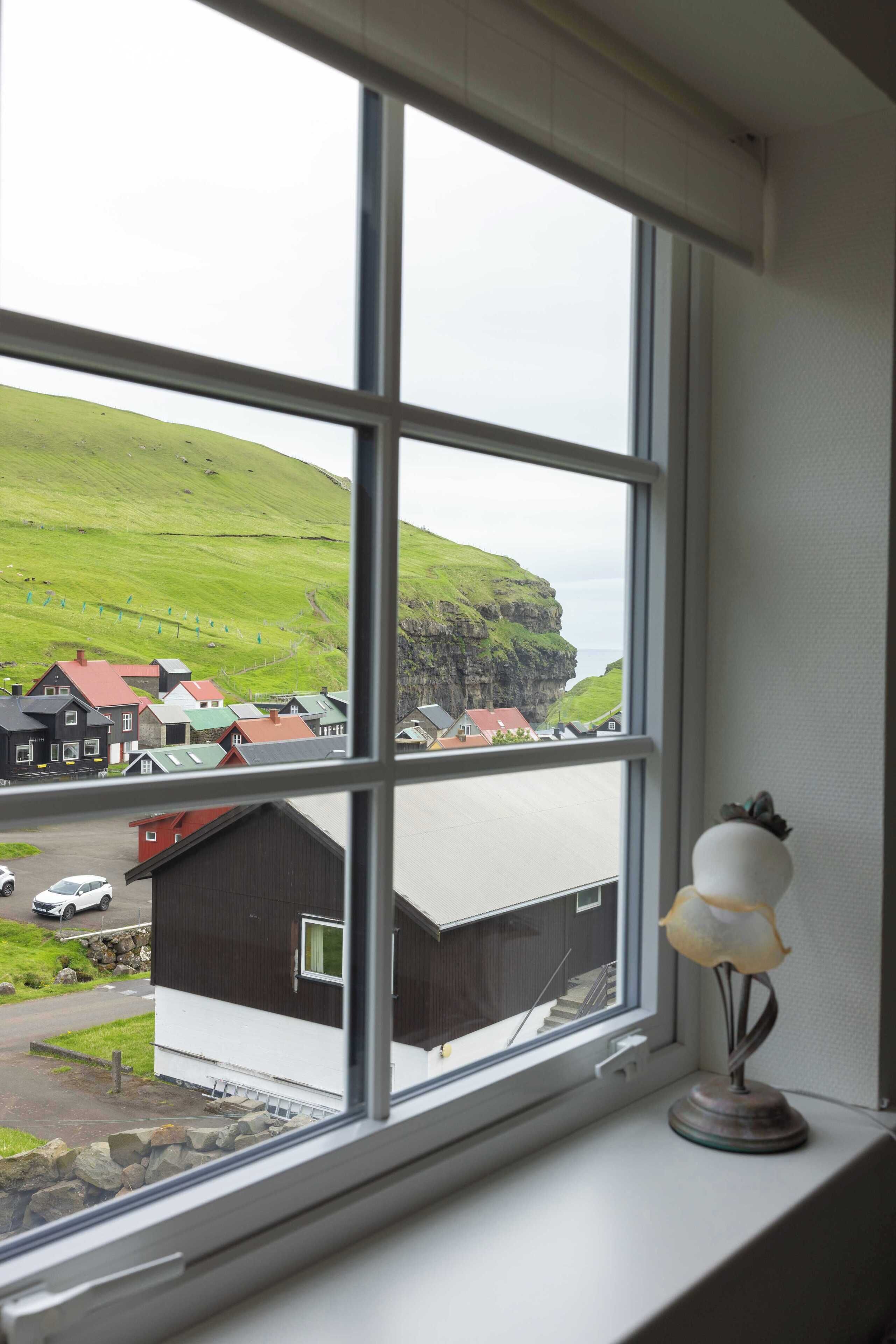 A window with a view of a green hill and buildings below.