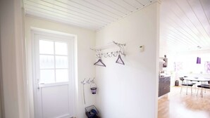 A room with a white door, a drying rack with clothes, a small basket with shoes, and a kitchen area with a dining table and chairs.