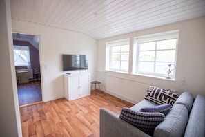 A living room with a sofa, a television on a cabinet, and a view of a balcony. - Summerhouse in Gjogv At the Edge of the Faroes (Gjógv)