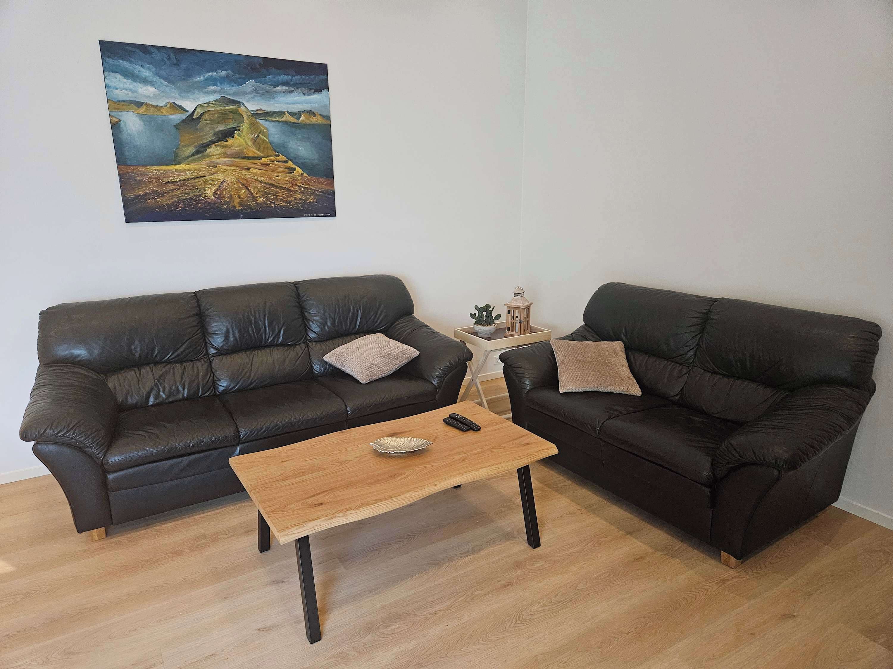 Un salon avec deux canapés en cuir noir, une table basse en bois et un tableau accroché au mur.