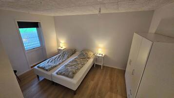 Une chambre à coucher avec un lit double, deux tables de chevet avec des lampes, une armoire et une fenêtre donnant sur une clôture.