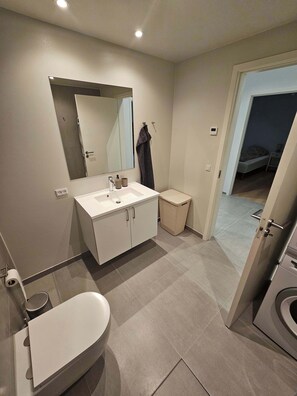 Une salle de bain moderne équipée de toilettes, d’un lavabo, d’un miroir et d’un espace douche.