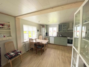 A kitchen with a dining area, wooden flooring, and a window with blinds. - Secluded Home with Mountain Views in Skalavik (Skálavík)