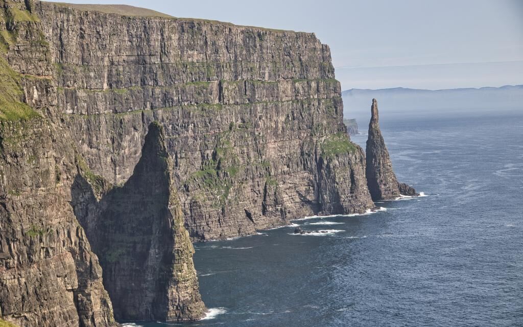 A coastal cliff with a narrow sea passage, rugged terrain, and a prominent rock formation.