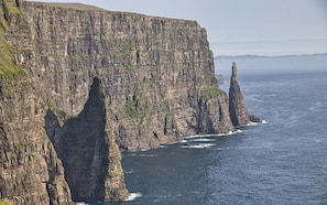 A coastal cliff with a narrow sea passage, rugged terrain, and a prominent rock formation.