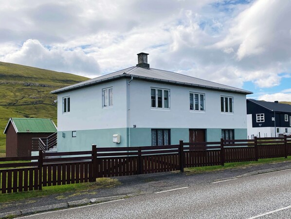 A two-story building with a flat roof, a visible number '19', and a fenced driveway. - Secluded Home with Mountain Views in Skalavik (Skálavík)