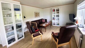 Ein Wohnzimmer mit einer Couch, zwei Sesseln, einem Couchtisch, einem Bücherregal und einem Fernseher.