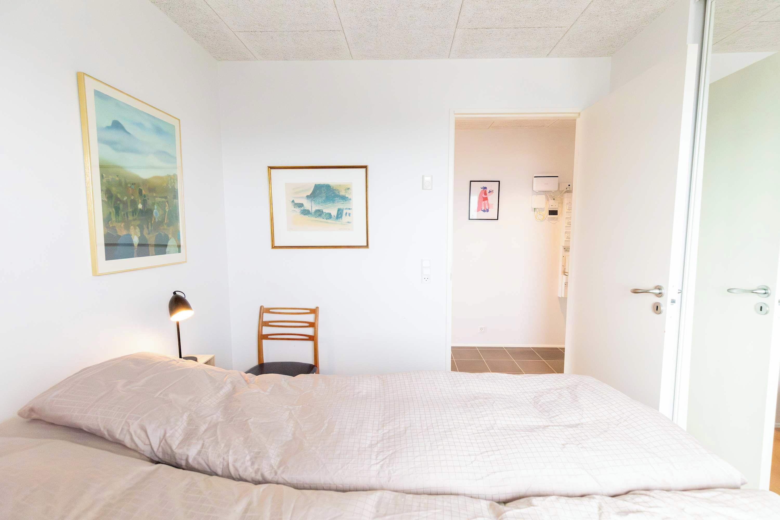 Een slaapkamer met een bed, een stoel en twee kunstwerken in lijsten aan de muur.