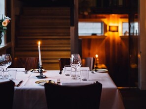 Ruokapöytä on katettu viinilaseilla, lautasilla ja aterimilla, ja pöydällä on kynttilä.