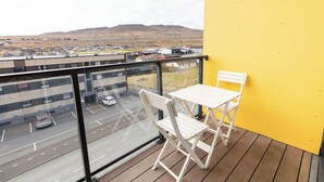 En balkong med ett bord och stolar, med utsikt över en parkeringsplats och byggnader, och därifrån ser man avlägsna kullar.