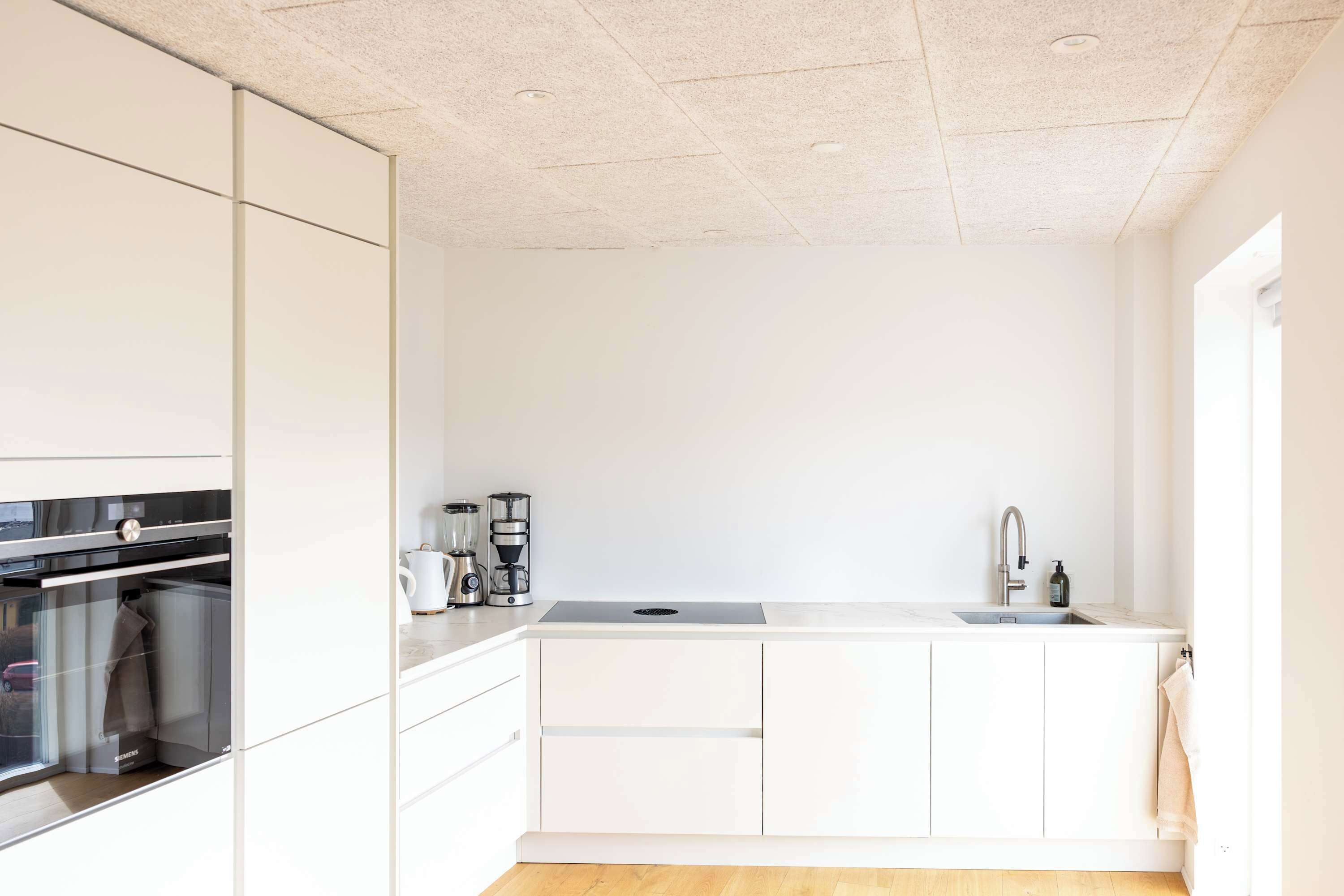Una cucina moderna con mobili bianchi, forno integrato, macchina da caffè e lavello.