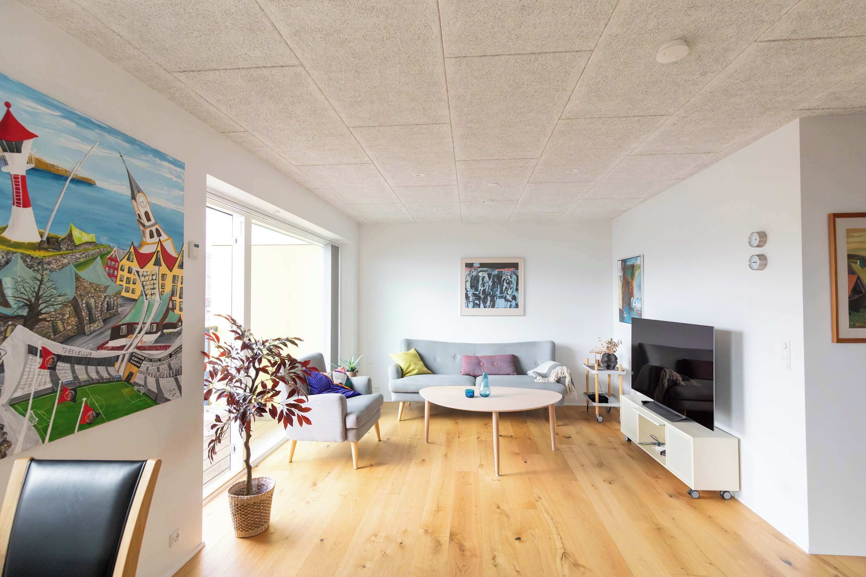 Ein modernes Wohnzimmer mit Sofa, Couchtisch und Fernseher. An der Wand hängt ein Gemälde und in der Ecke steht eine Pflanze.