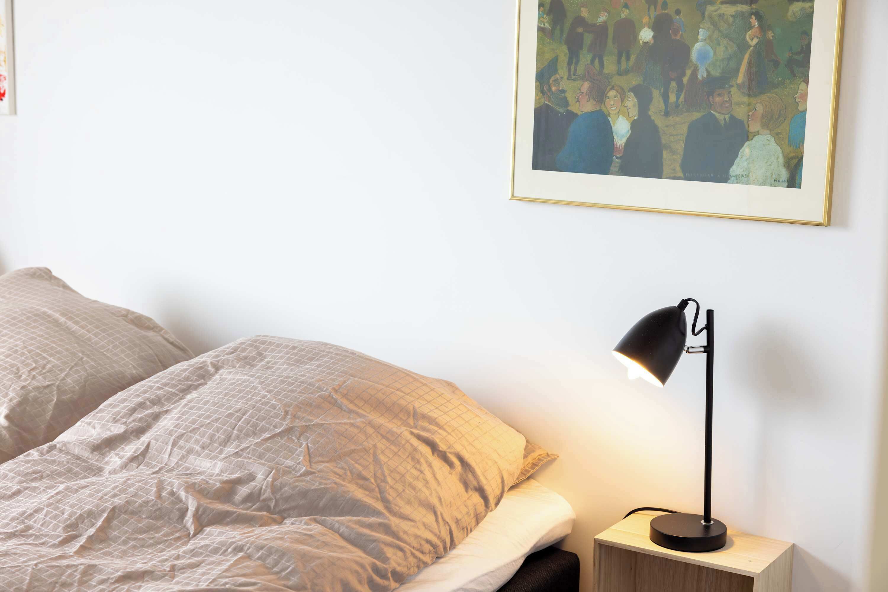 Ein Schlafzimmer mit einem Bett, einem Nachttisch, einer Lampe und einem Bild an der Wand.