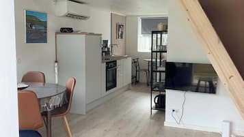Une cuisine moderne avec des meubles blancs, un coin repas doté d’une table ronde et de chaises, et un espace en mezzanine avec un escalier en bois.