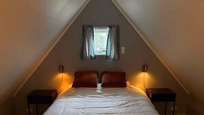 Ein Schlafzimmer mit einem großen Bett, zwei Nachttischen, einem Fenster mit Vorhängen und einer geneigten Decke.