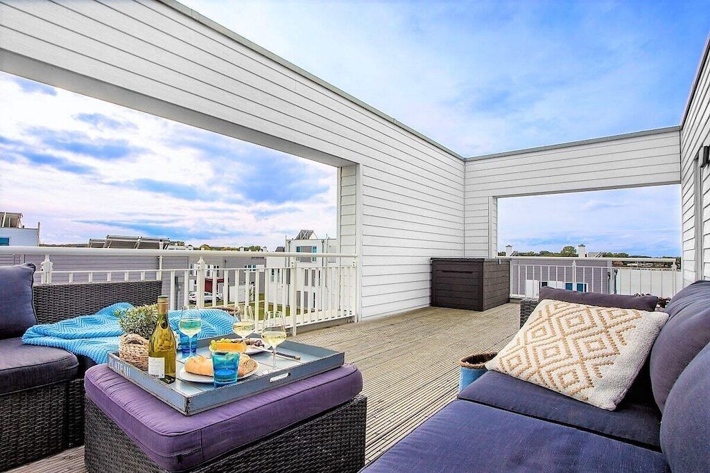 An outdoor deck with a seating area, a table with drinks and snacks, and a view of the surrounding buildings.