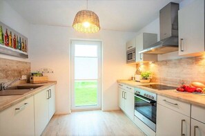 A modern kitchen with white cabinetry, a built-in oven, and a large window. - Holiday home in Kappeln with swimming pool (Kappeln)