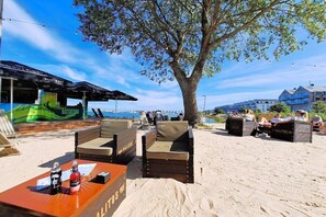 Un espacio de descanso frente a la playa con una mesa, sillas y un árbol que da sombra.