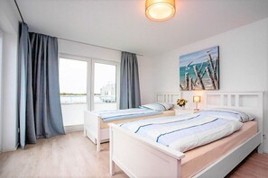 Habitación de hotel con dos camas, un ventanal con cortinas, un cuadro en la pared y una mesita de noche con lámpara.