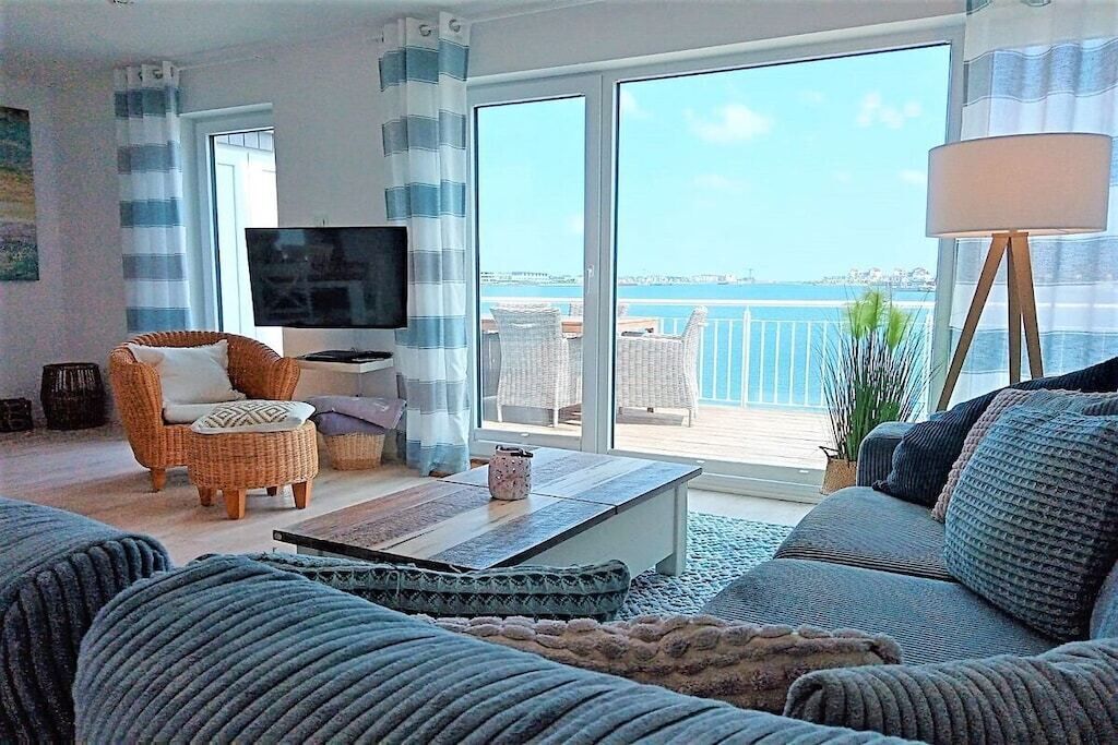 A living room with a television, wicker furniture, a sofa, and a view of the sea.