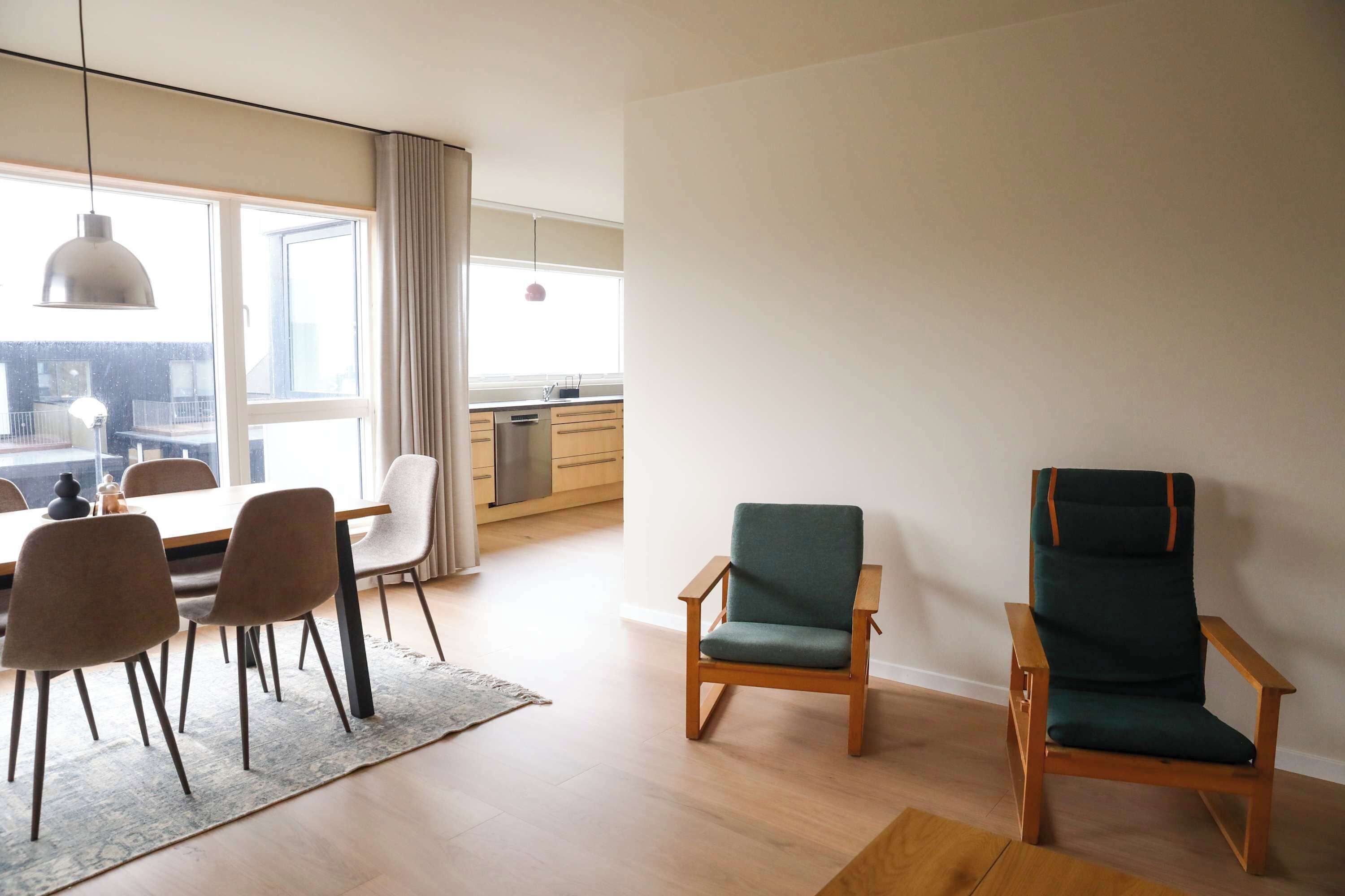 Ein modernes Wohnzimmer mit Essbereich, zwei Stühlen, einem Teppich und Blick auf die Stadt durch große Fenster.