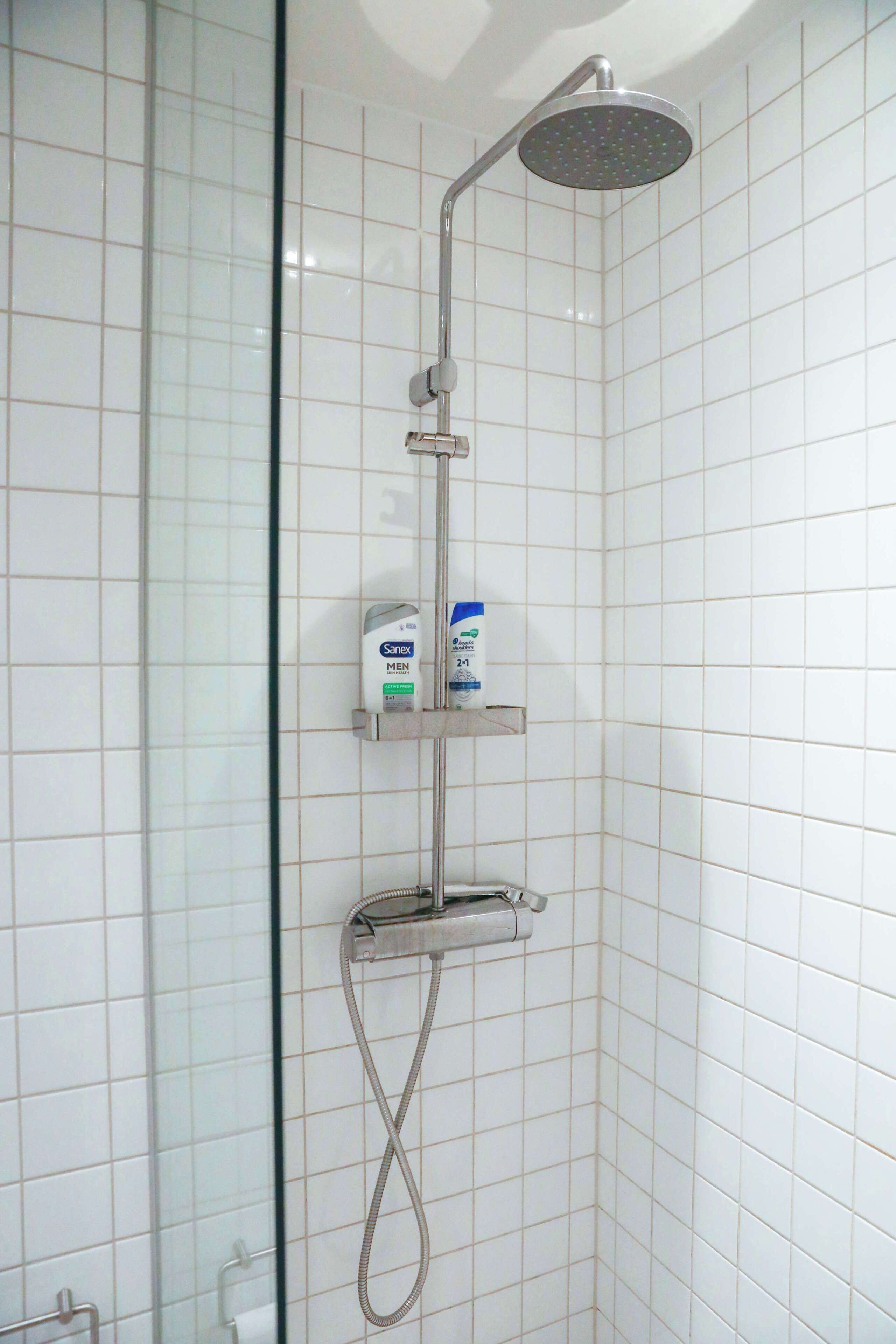 A shower with a handheld showerhead, a handheld shower attachment, and a soap dispenser on a shelf.