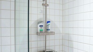 Une douche équipée d’un pommeau de douche à main, d’un flexible de douche et d’un distributeur de savon fixé sur une étagère.