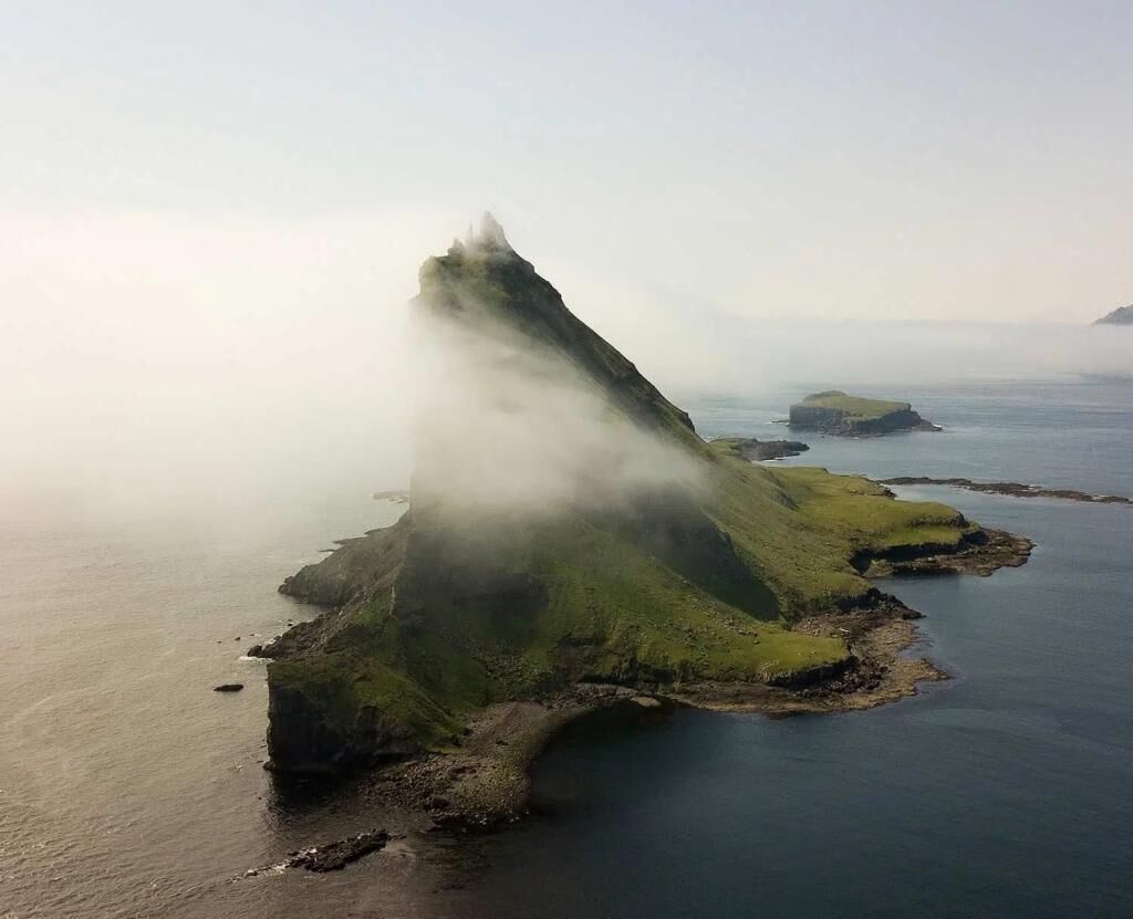 A coastal landscape with a prominent green hill and a body of water.