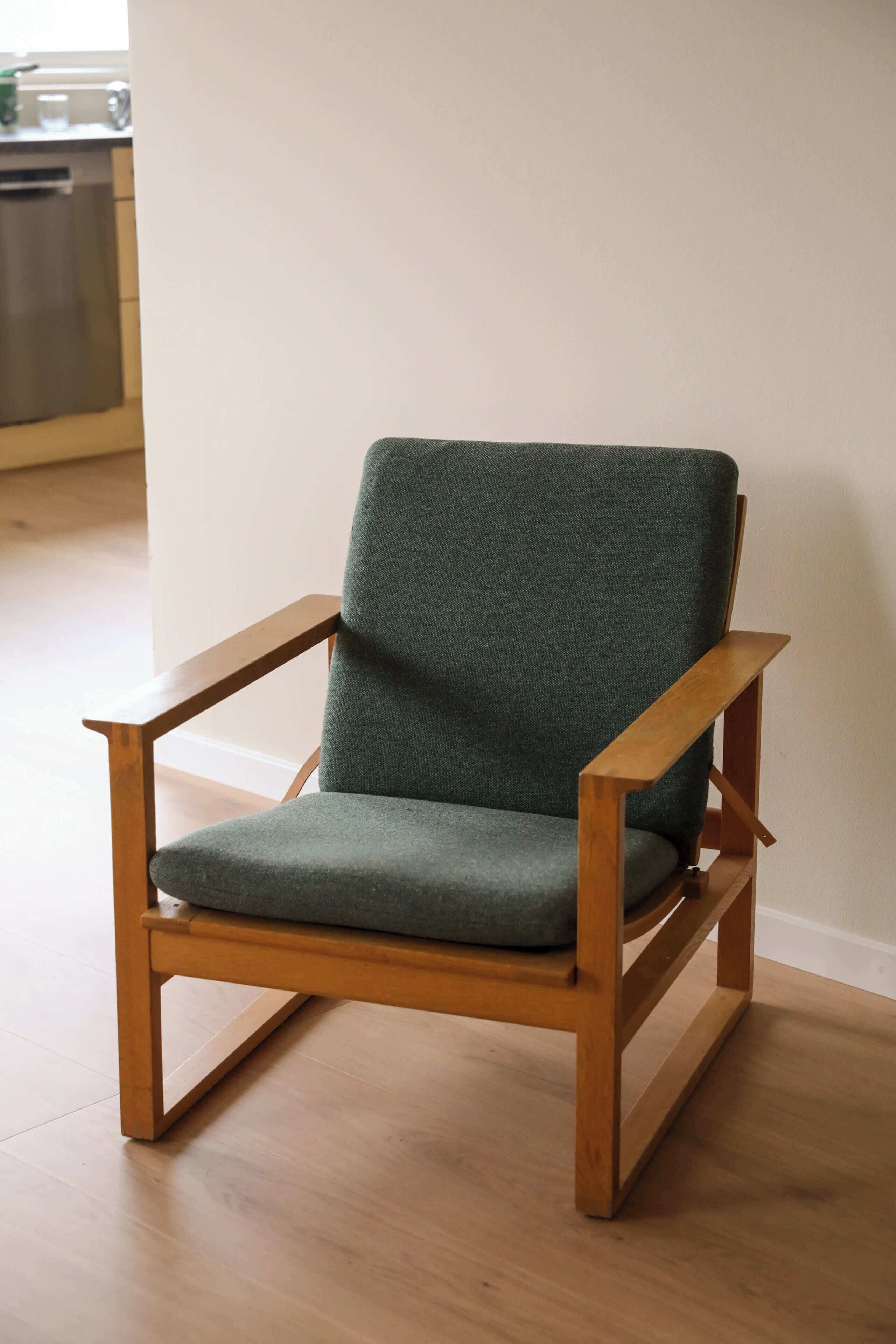 A wooden chair with a green upholstered seat and backrest.