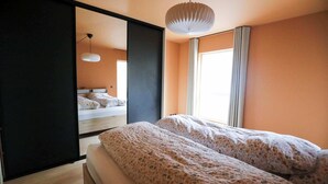 Une chambre à coucher avec un lit, un grand miroir et un luminaire suspendu.